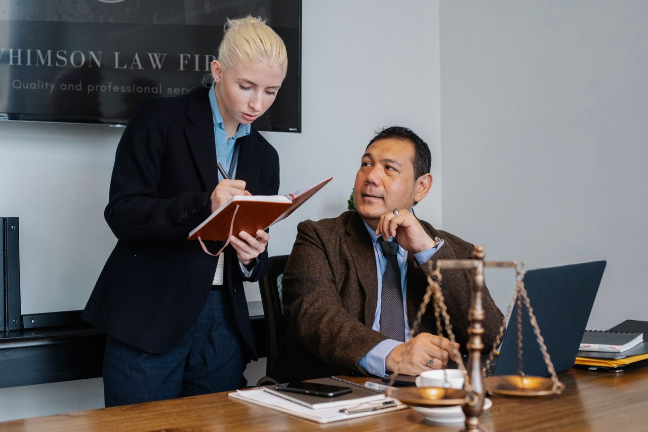 about-img Young female secretary in formal clothes taking notes in notebook and taking to serious Asian male manager while working in law firm together