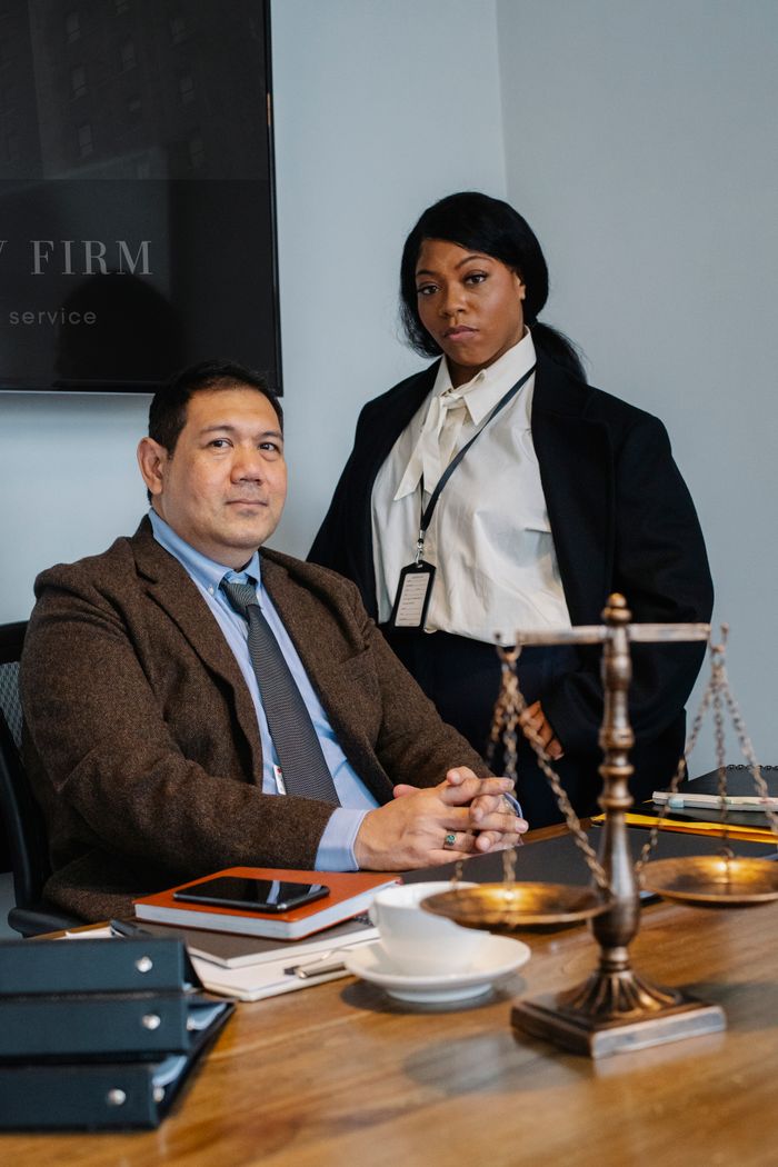 portfolio-img-04 Focused young black woman in formal clothes standing near male ethnic colleague at wooden table with documents and justice scale during work in law firm