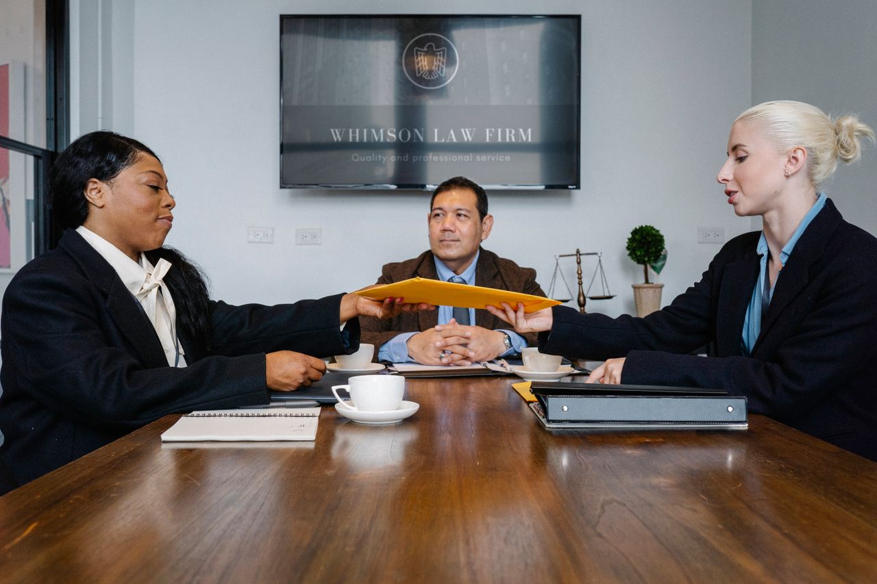 hero-gallery-02 Group of cheerful diverse colleagues discussing court decision at table with notepad and cup