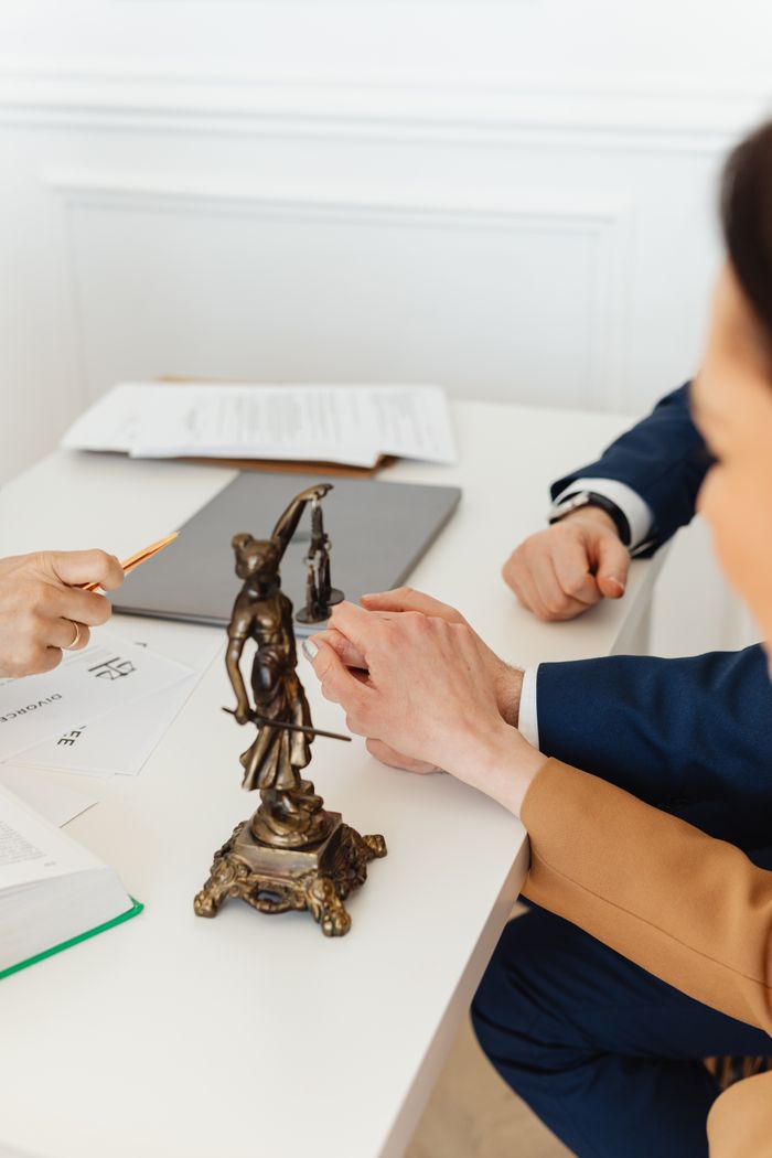 portfolio-img-02 Legal professionals discussing documents with Lady Justice statue on desk.