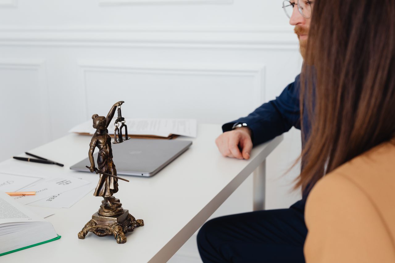 portfolio-img-01 Professional setting with lawyers and Lady Justice statue discussing legal documents.