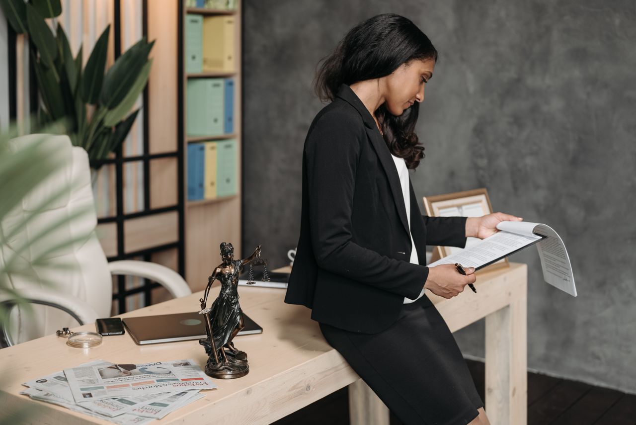 about-img A professional woman in a business suit reviews legal documents at her office desk.